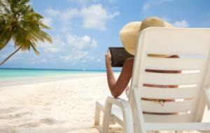 Woman with tablet computer on the beach sitting in the deck chair